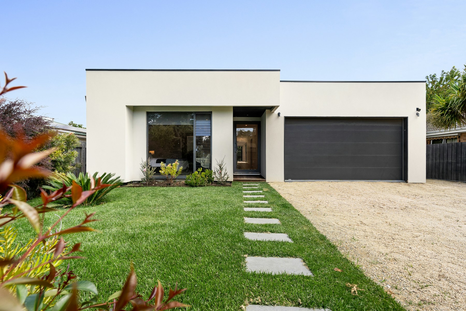 Modern white residence with a wide black sectional garage door and landscaped front garden.